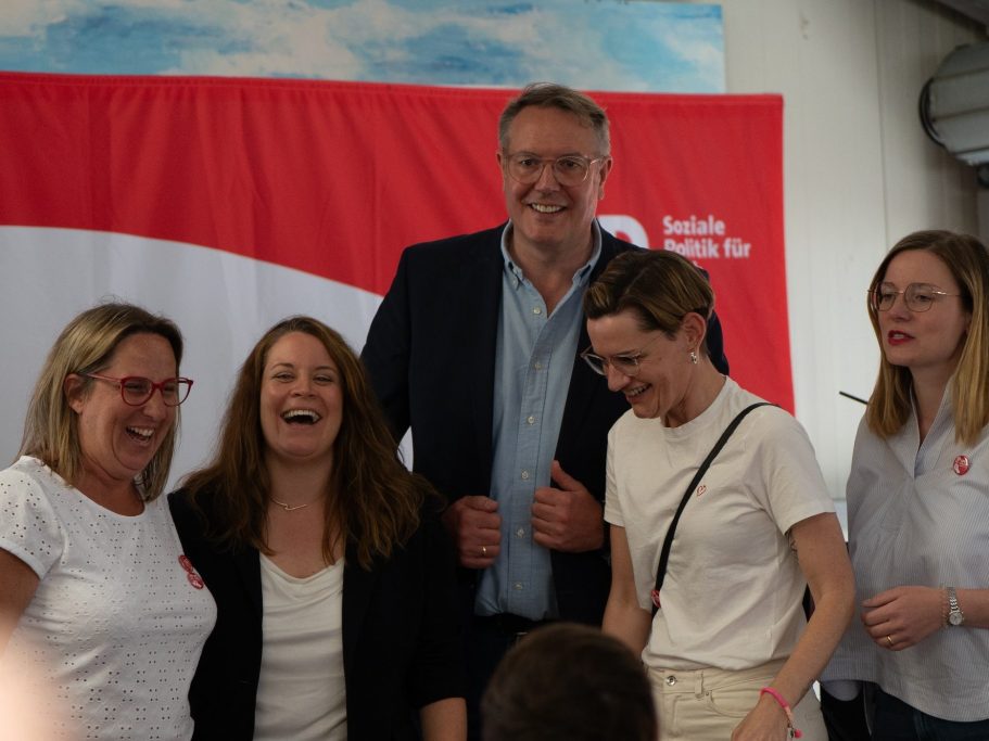 Fünf Personen stehen zusammen, lachen und posieren vor einem roten Banner.