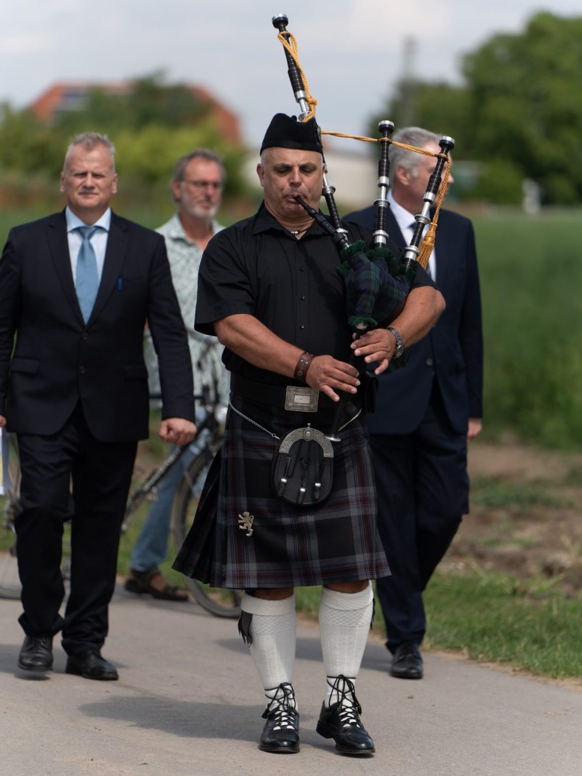 Ein Mann in Schottenrock spielt Dudelsack, während er mit anderen Personen geht.