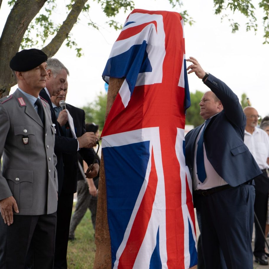 Eine Statue wird mit einer britischen Flagge wird enthüllt, während mehrere Personen zuschauen.