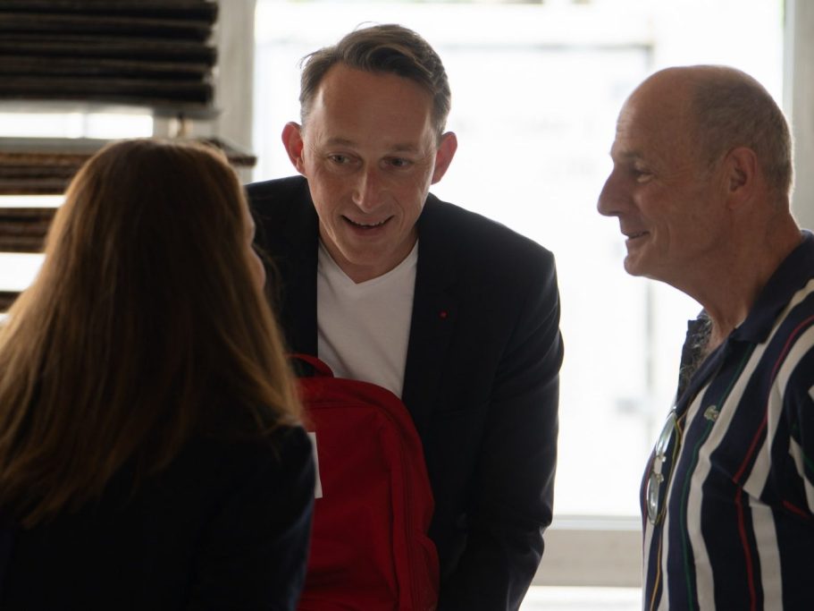 Drei Personen bei einem Gespräch, einer hält einen roten Rucksack.