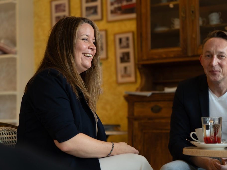 Zwei Personen in einem Café, die miteinander sprechen, Getränke auf dem Tisch.