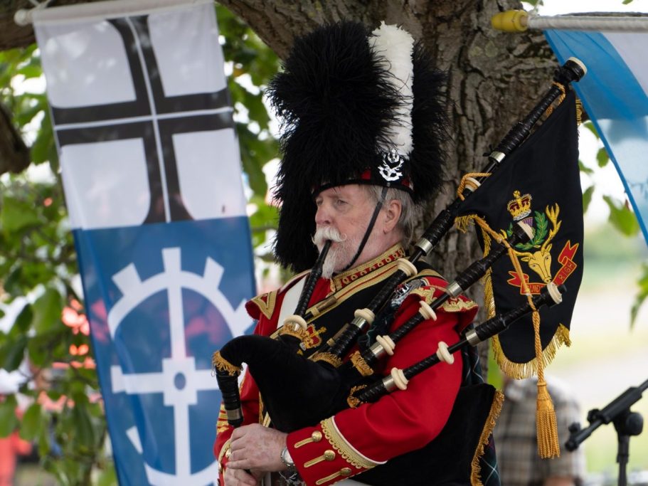 Ein uniformierter Soldat spielt Dudelsack unter einem Baum.